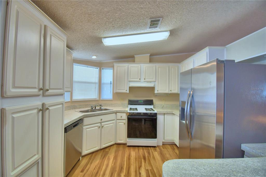 A kitchen features white cabinets, stainless steel appliances, a corner sink, and wood-look flooring — 6086 SOUTHERN OAKS DRIVE, WINTER HAVEN, FL