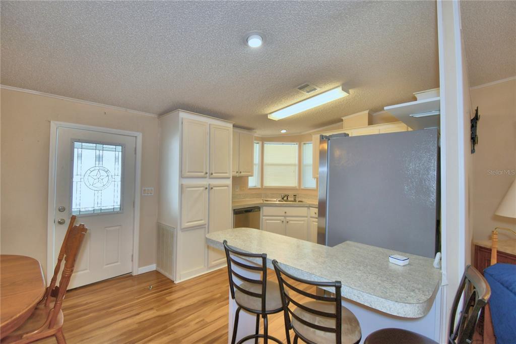 A kitchen features white cabinets, a breakfast bar, stainless steel appliances, and wood-look flooring — 6086 SOUTHERN OAKS DRIVE, WINTER HAVEN, FL