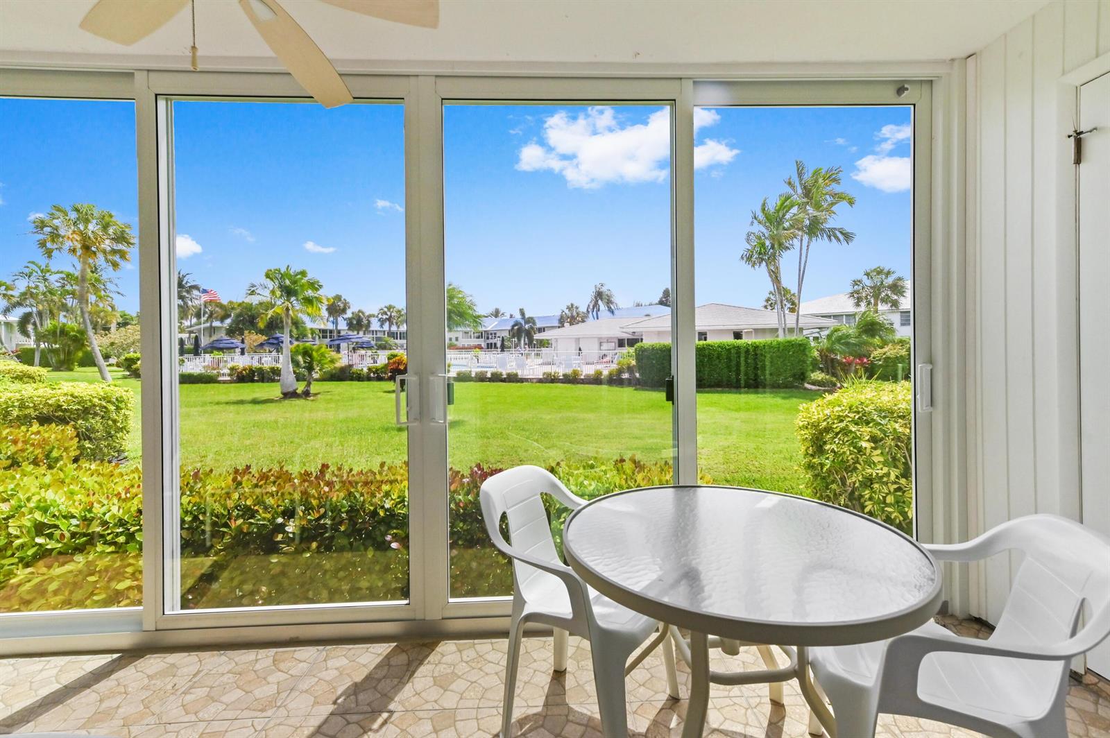 A sunroom features a glass-topped table, white chairs, and sliding doors overlooking a grassy courtyard — 5540 N Ocean Boulevard # 107, Ocean Ridge FL 33435, OCEAN RIDGE, FL