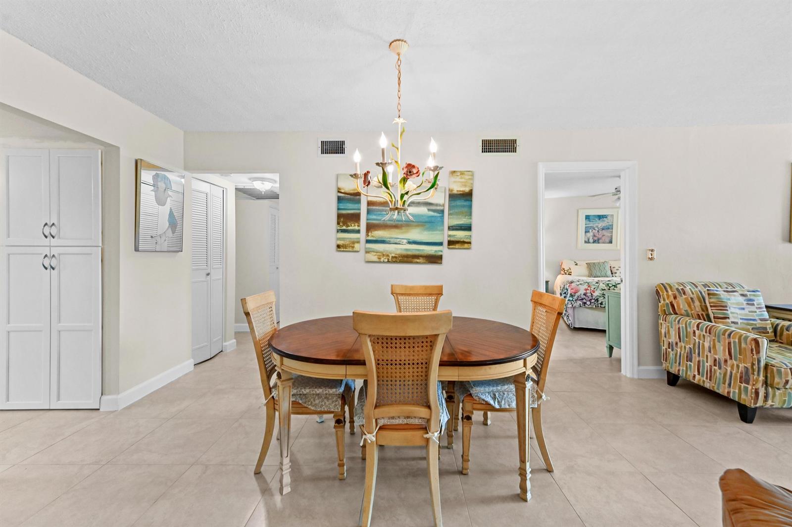 A dining area features a round wooden table, four chairs, and a floral chandelier — 5540 N Ocean Boulevard # 107, Ocean Ridge FL 33435, OCEAN RIDGE, FL