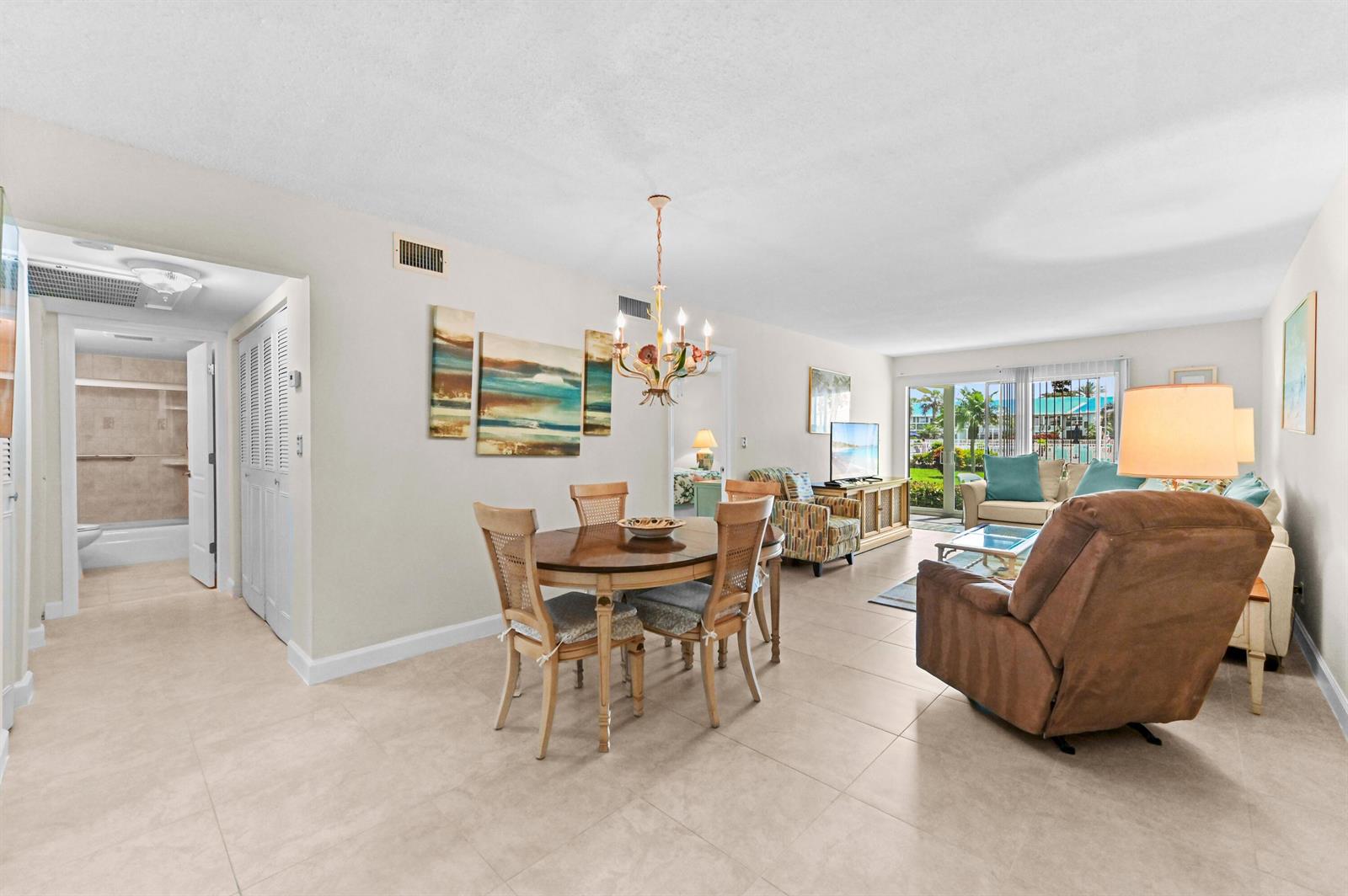 An open-concept living and dining area with tile floors, a chandelier, and a sliding door — 5540 N Ocean Boulevard # 107, Ocean Ridge FL 33435, OCEAN RIDGE, FL