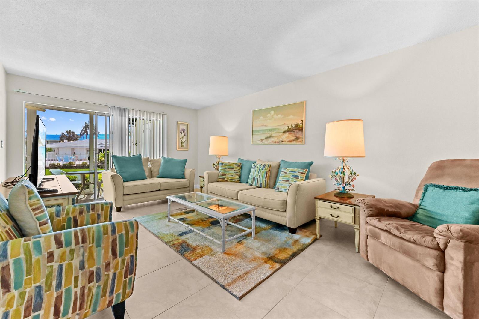A living room features beige sofas, a patterned armchair, a glass coffee table, and tile flooring — 5540 N Ocean Boulevard # 107, Ocean Ridge FL 33435, OCEAN RIDGE, FL