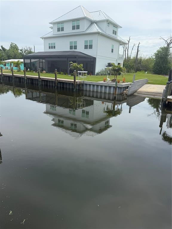 A three-story white house sits along a canal with a screened porch and boat ramp — 10460 RAYMOND STREET, ENGLEWOOD, FL