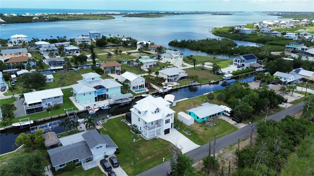 An aerial view shows a coastal neighborhood with houses, canals, and a nearby bay — 10460 RAYMOND STREET, ENGLEWOOD, FL