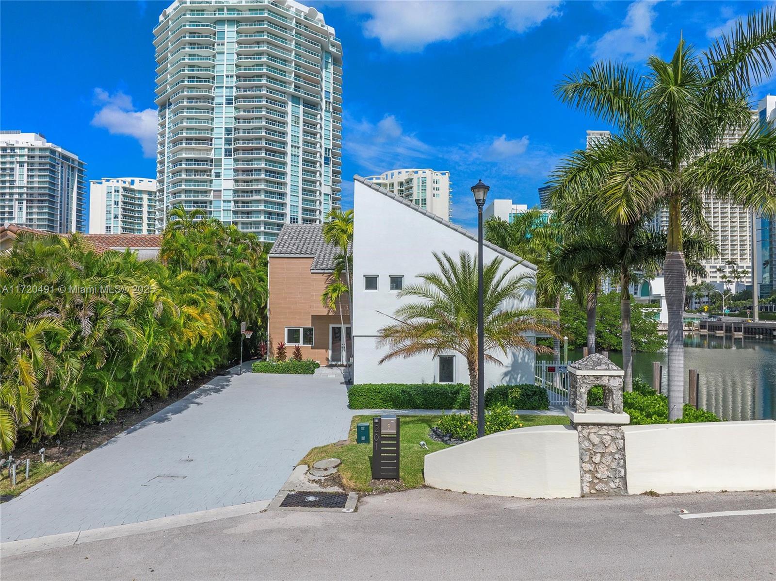 A white house with a slanted roof sits next to a canal with high-rise buildings behind — 201 Atlantic Ave, Sunny Isles Beach FL 33160, SUNNY ISLES BEACH, FL