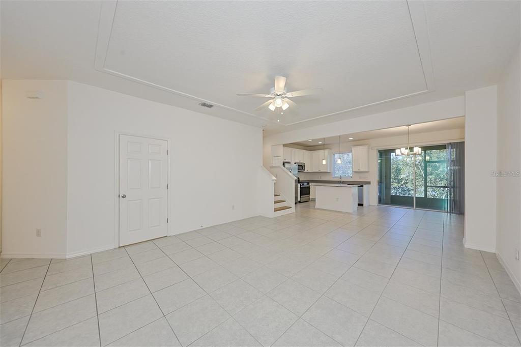 A bright, open-concept living area with white tile floors, a tray ceiling, and kitchen — 6222 CAMINO DRIVE, APOLLO BEACH, FL