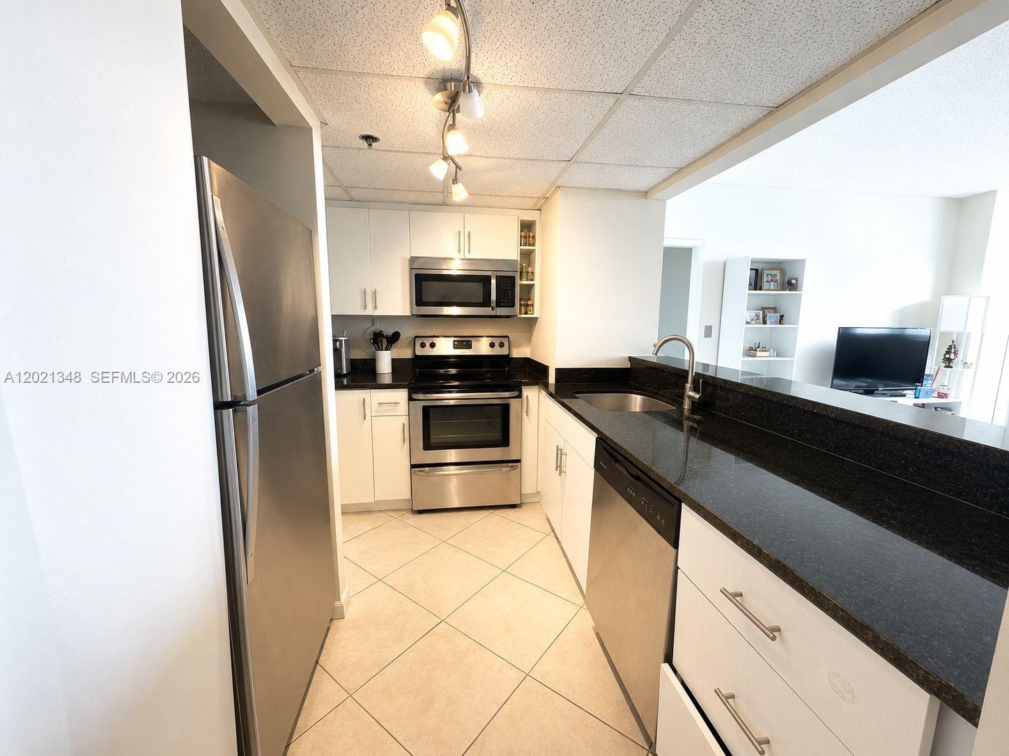A galley kitchen features white cabinets, stainless steel appliances, and black granite countertops — 540 Brickell Key Dr # 1801, Miami FL 33131, MIAMI, FL