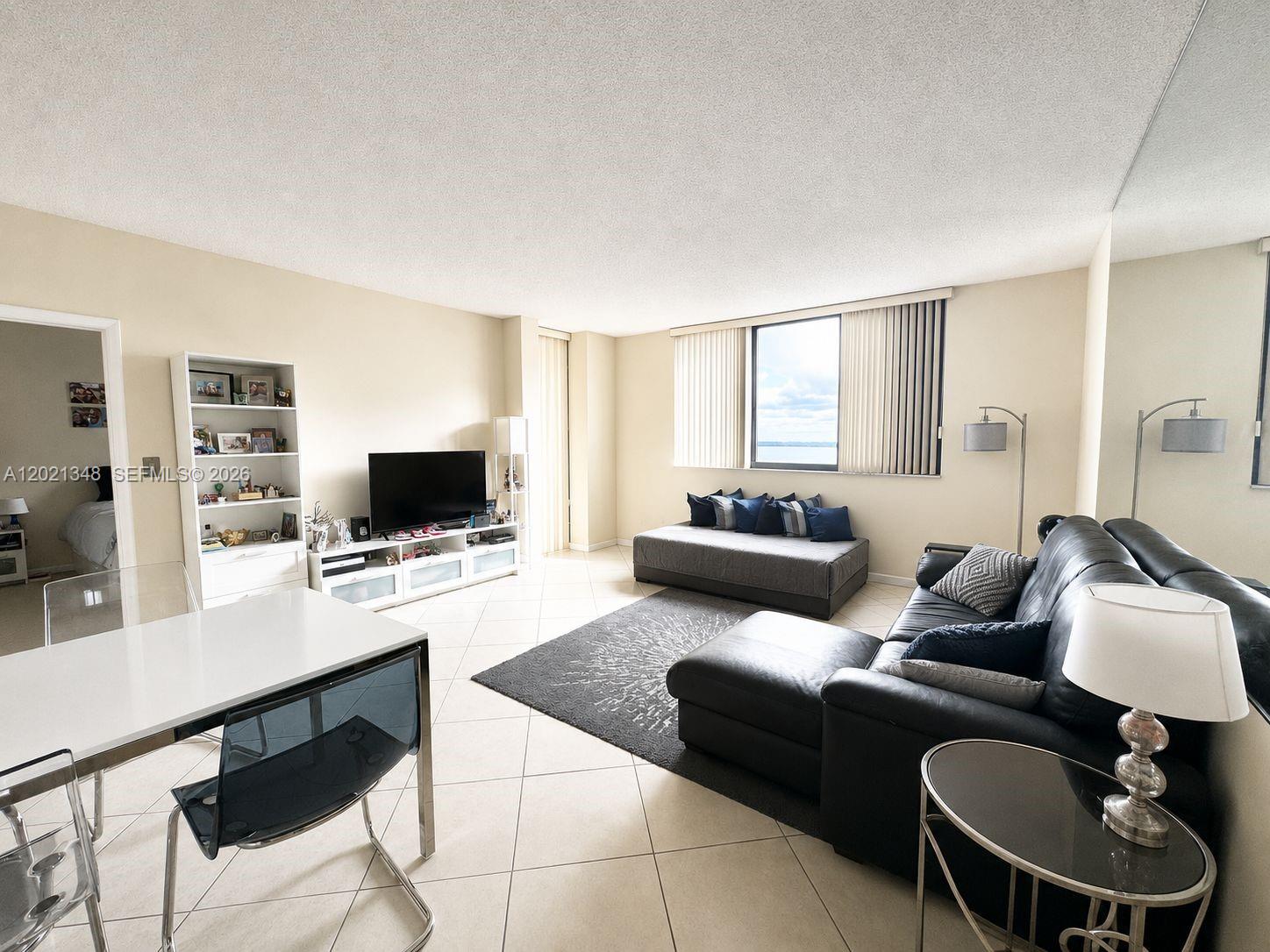 A living room features tile floors, a black sectional sofa, and a large window view — 540 Brickell Key Dr # 1801, Miami FL 33131, MIAMI, FL