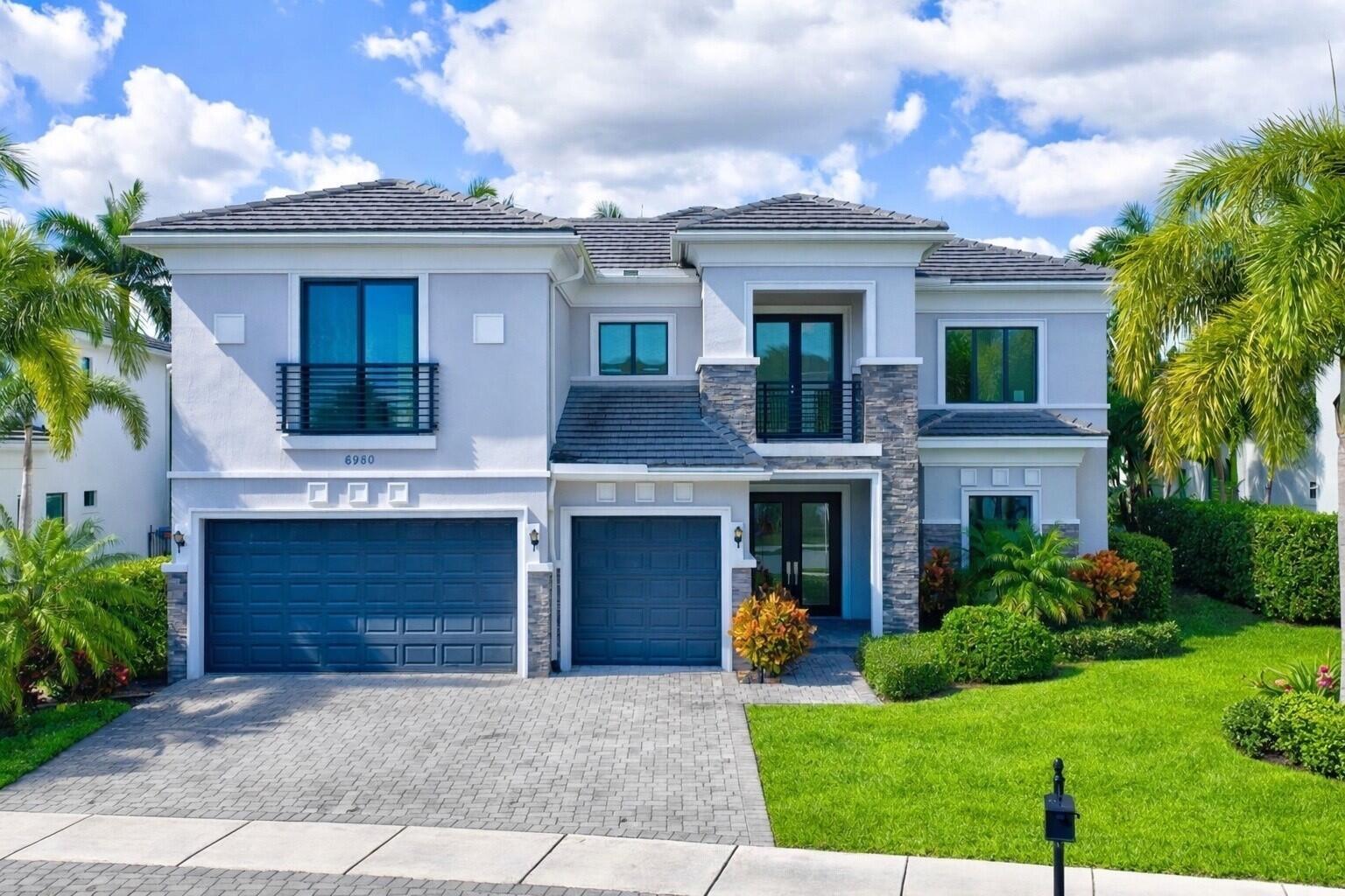 A two-story house with a gray exterior, stone accents, two garage doors, and palm trees — 6980 NW 28th Avenue, Boca Raton FL 33496, BOCA RATON, FL