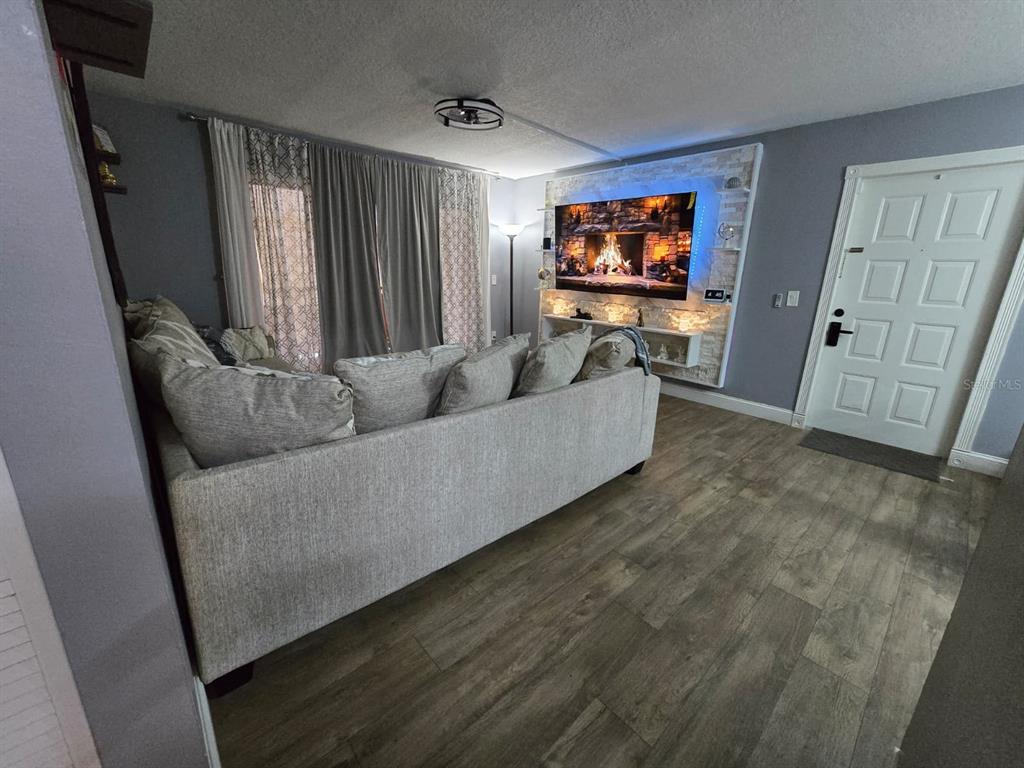 A living room features a gray sofa, wood-look flooring, and a stone-accented wall with a television — 1624 S PINE RIDGE UNIT D2, SANFORD, FL