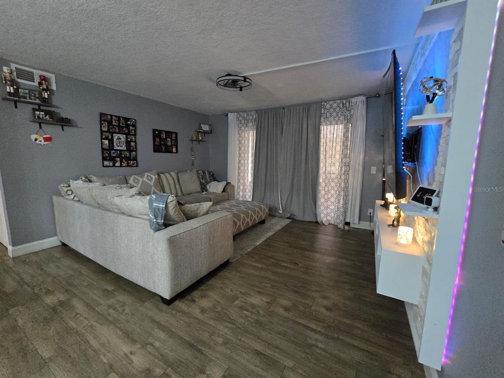 A living room features gray walls, wood-look flooring, a sectional sofa, and a stone accent wall — 1624 S PINE RIDGE UNIT D2, SANFORD, FL