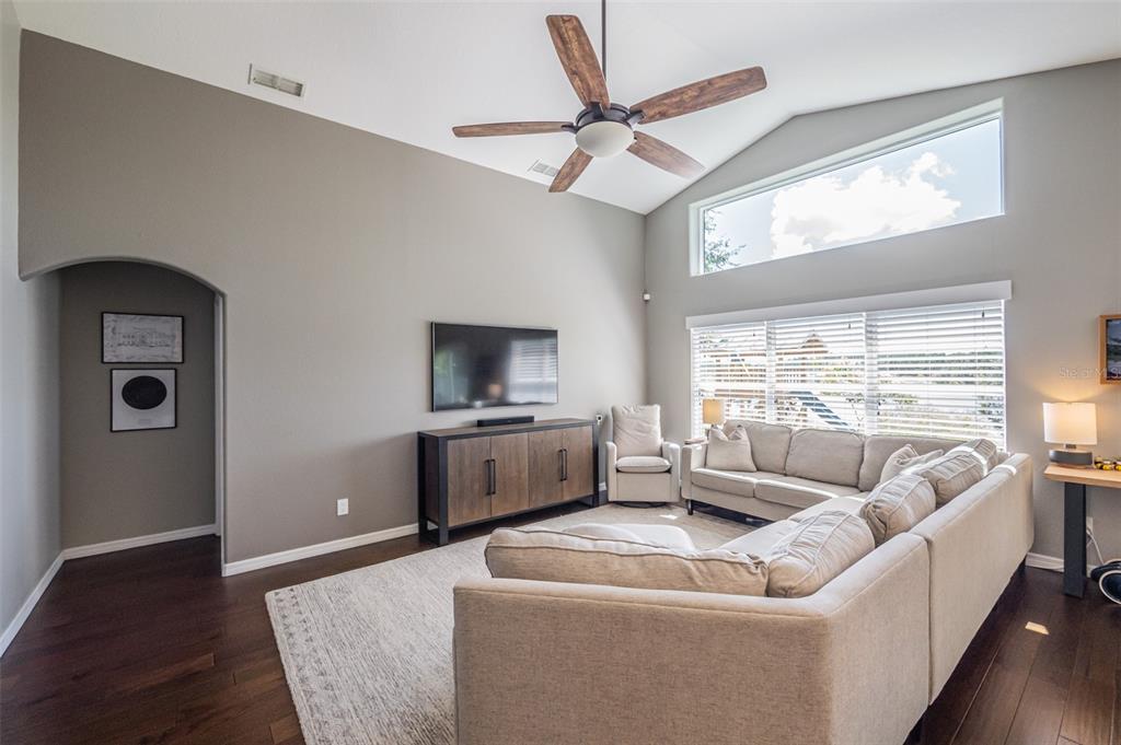 A living room with vaulted ceilings, a sectional sofa, a television, and dark wood flooring — 538 WINDSOR ESTATES DRIVE, DAVENPORT, FL