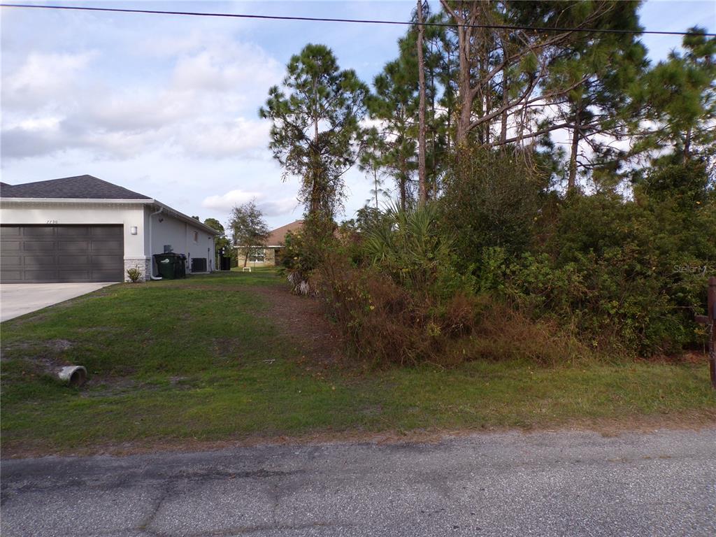 A vacant, grassy residential lot sits next to a house with a gray garage door — MEROLLA ROAD, NORTH PORT, FL