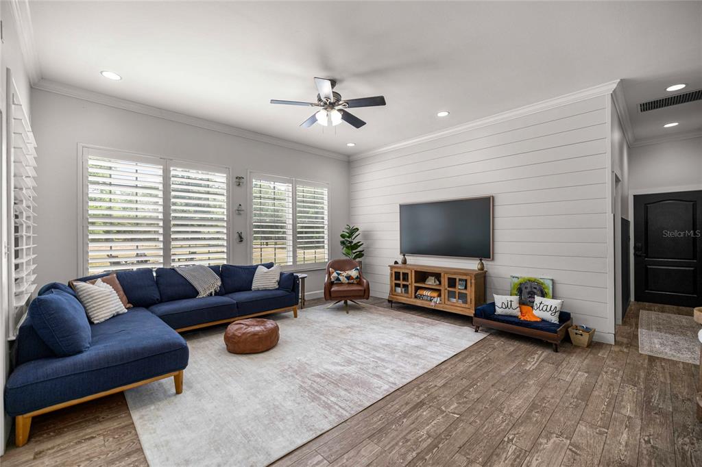 A living room features a blue sectional sofa, shiplap wall, and wood-look tile flooring — 25162 NW 204TH PLACE, HIGH SPRINGS, FL