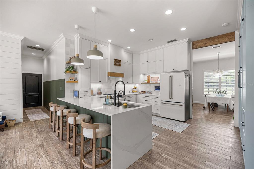 A modern kitchen features white cabinetry, a waterfall island with bar seating, and wood flooring — 25162 NW 204TH PLACE, HIGH SPRINGS, FL