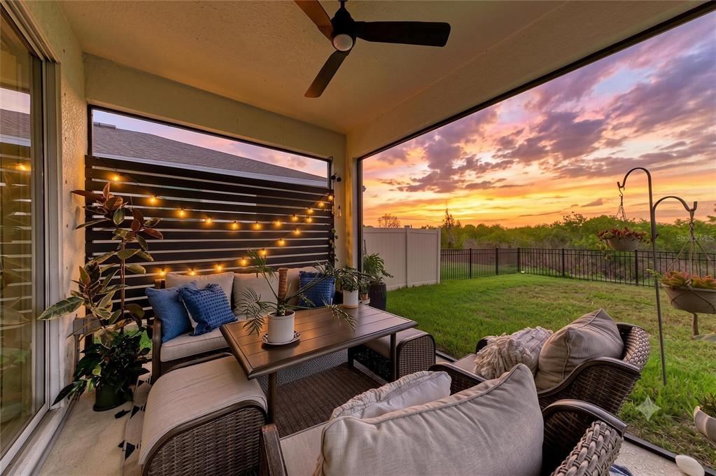 A screened-in patio features outdoor furniture, string lights, and a view of a sunset — 10815 CHARLOTTE DRIVE, PARRISH, FL