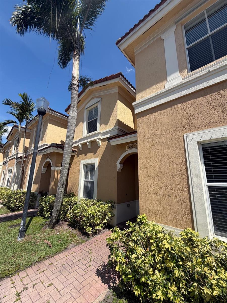 An exterior view of a two-story tan stucco townhouse with a brick walkway and palm trees — 3023 SW 129th Ter # 155, Miramar FL 33027, MIRAMAR, FL