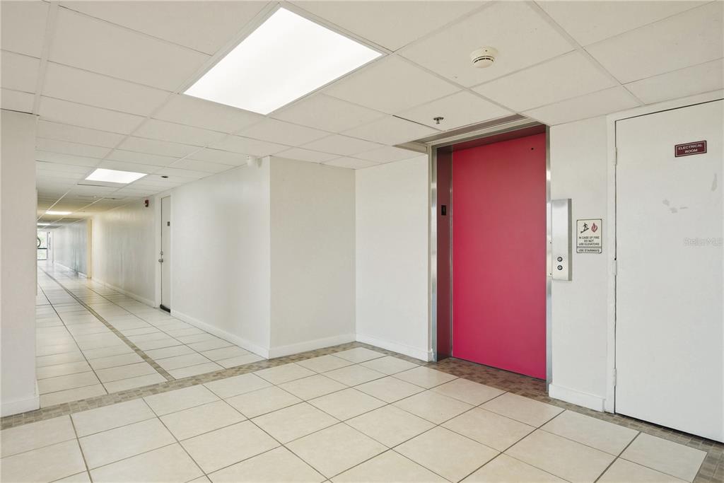 A hallway with white tiled floors, a bright pink elevator door, and a white door — 701 S MADISON AVENUE UNIT 420, CLEARWATER, FL