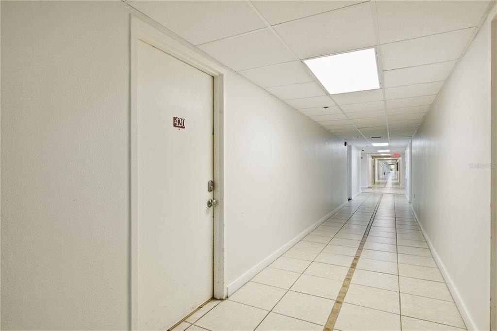 A long, tiled hallway features a white door labeled 420 and a drop ceiling — 701 S MADISON AVENUE UNIT 420, CLEARWATER, FL
