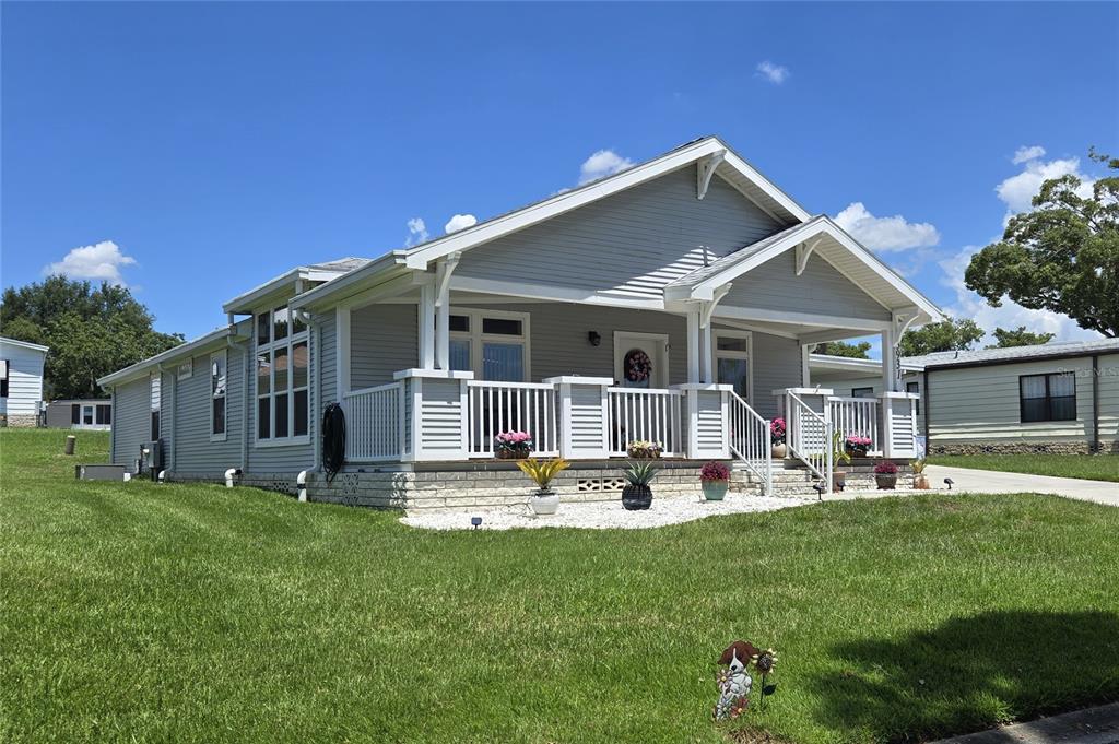 A light gray house with a covered front porch and white railings sits on grass — 3931 COHEN DRIVE UNIT 734, ZELLWOOD, FL