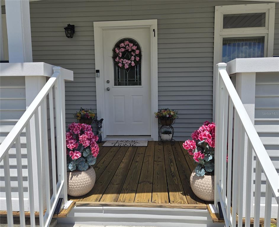 A wooden front porch features a white door with a wreath and potted pink flowers — 3931 COHEN DRIVE UNIT 734, ZELLWOOD, FL