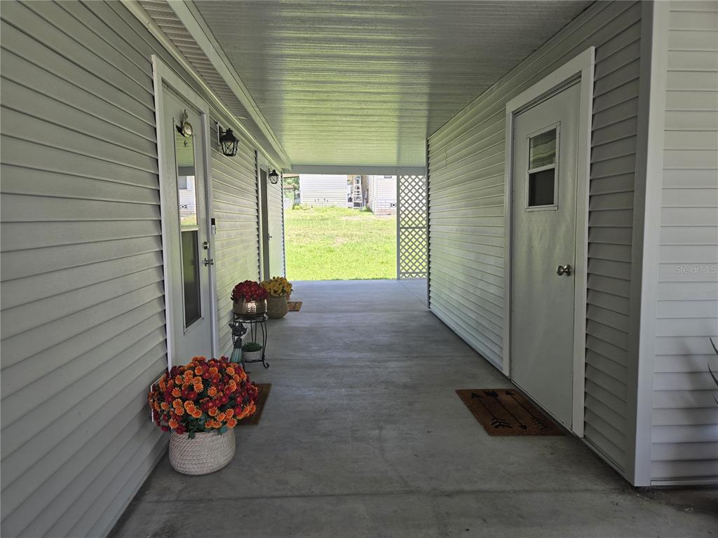 A covered concrete walkway sits between two exterior walls with white doors and potted flowers — 3931 COHEN DRIVE UNIT 734, ZELLWOOD, FL