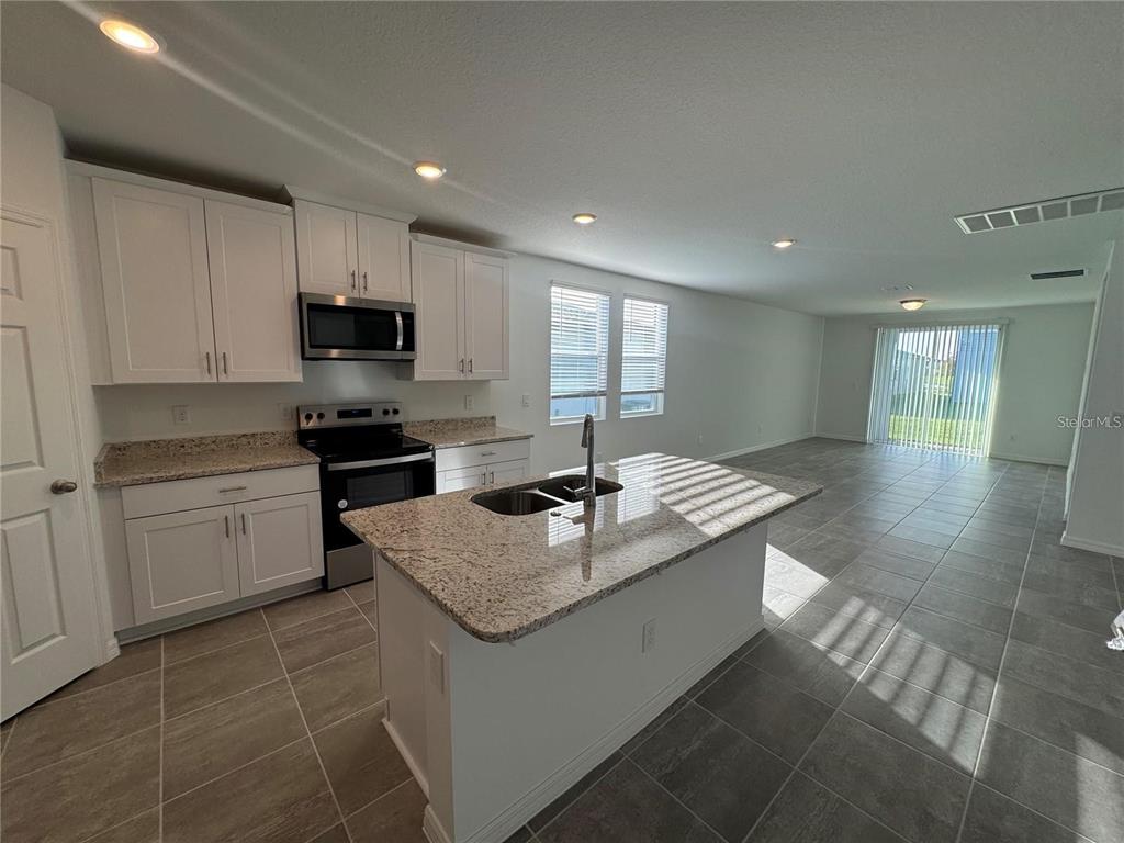 A kitchen with white cabinets, granite countertops, and an island opens to a living area — 4552 PICKEREL WEED WAY, ST CLOUD, FL