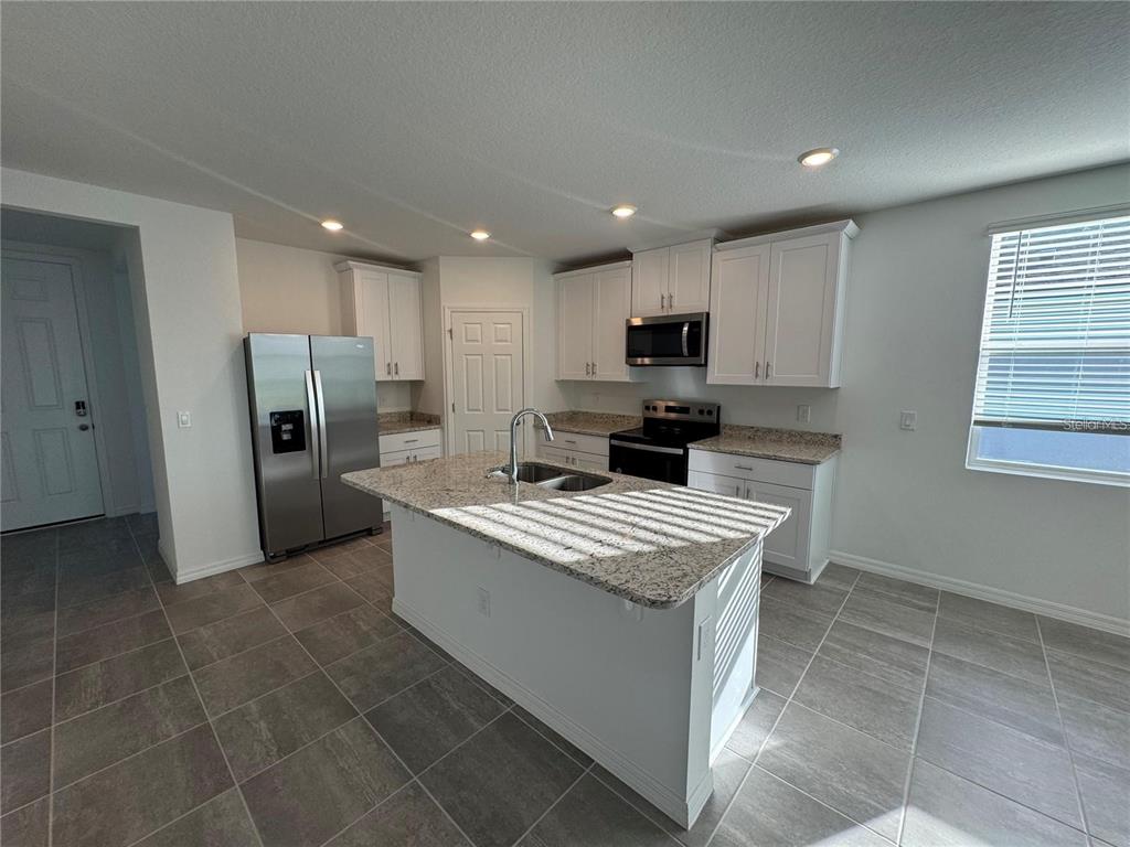 A kitchen features white cabinets, granite countertops, a center island, and stainless steel appliances — 4552 PICKEREL WEED WAY, ST CLOUD, FL