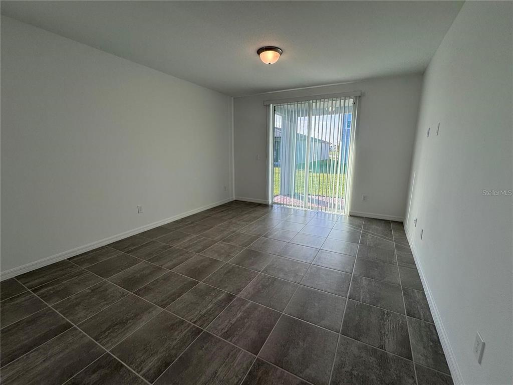 An empty room features gray tile flooring, white walls, and a sliding glass door — 4552 PICKEREL WEED WAY, ST CLOUD, FL