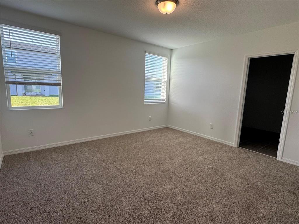An empty bedroom features beige carpeting, white walls, two windows with blinds, and a doorway — 4552 PICKEREL WEED WAY, ST CLOUD, FL