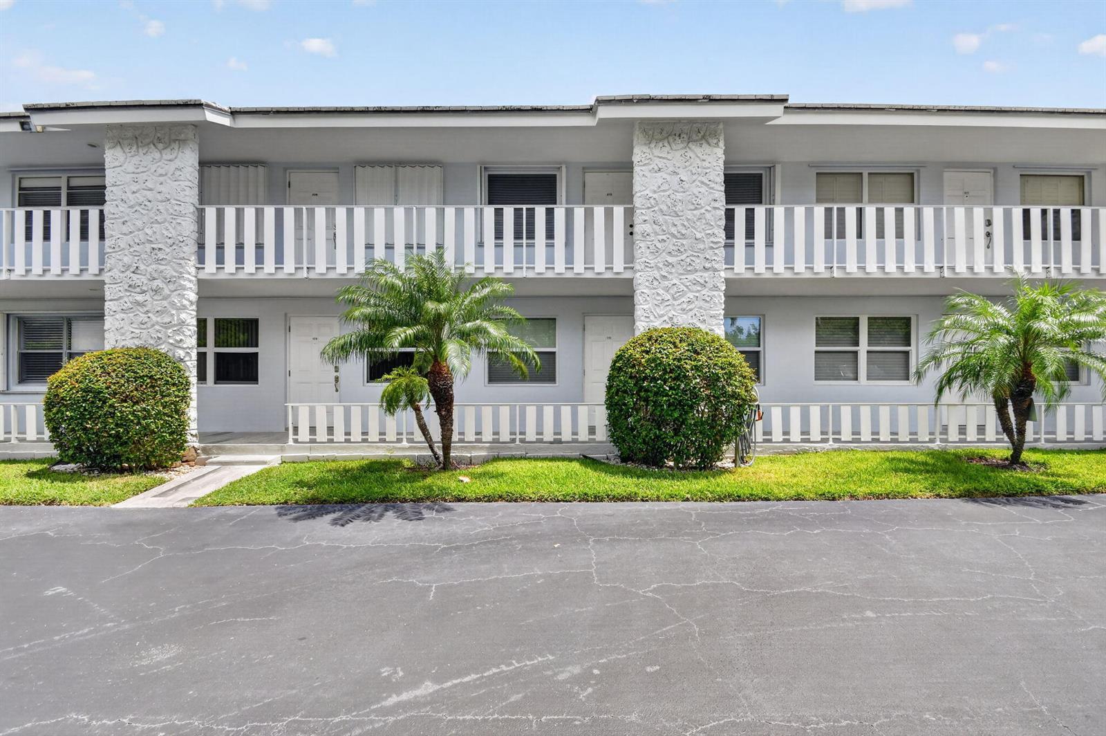 A two-story apartment building features white railings, textured stone pillars, and palm trees — 5520 N Ocean Boulevard N # 110, Ocean Ridge FL 33435, OCEAN RIDGE, FL
