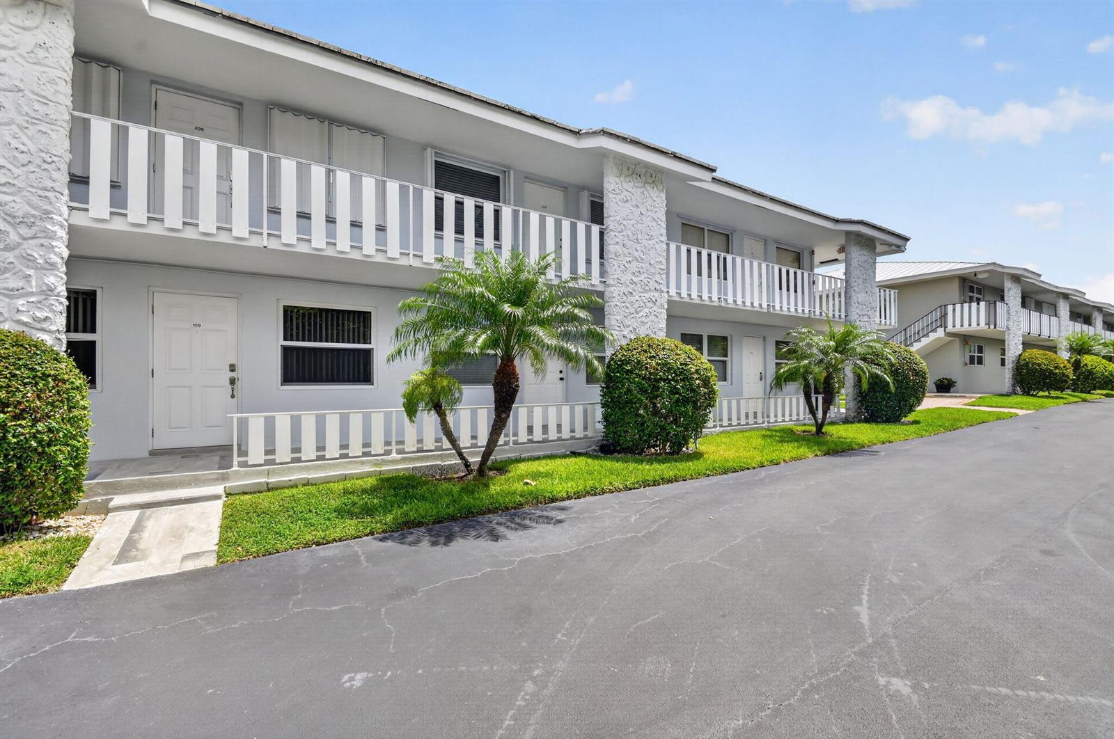 A two-story apartment building features white railings, textured stone pillars, and a paved driveway — 5520 N Ocean Boulevard N # 110, Ocean Ridge FL 33435, OCEAN RIDGE, FL