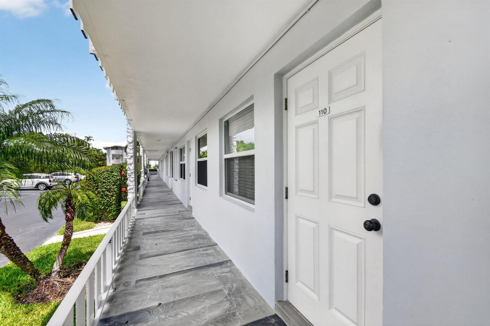 A white exterior door numbered 110 opens onto a covered walkway with gray tiled flooring — 5520 N Ocean Boulevard N # 110, Ocean Ridge FL 33435, OCEAN RIDGE, FL