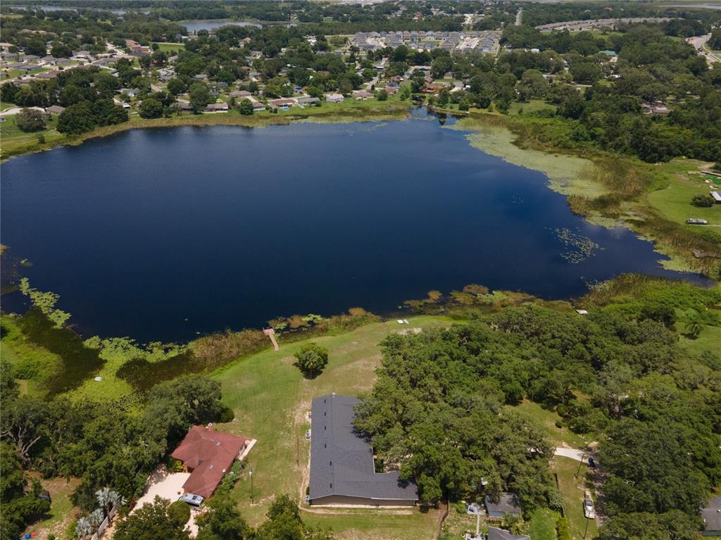 An aerial view shows a house with a dark roof situated beside a large lake — 81 N CAROL AVENUE, MASCOTTE, FL