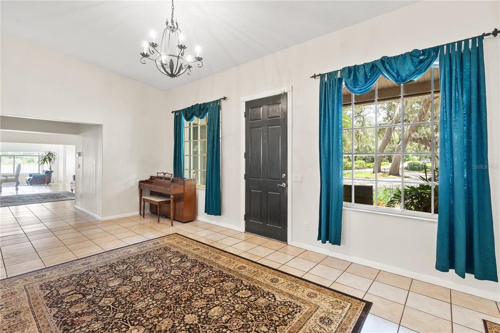 A tiled entryway features a piano, a large area rug, and teal curtains over windows — 81 N CAROL AVENUE, MASCOTTE, FL