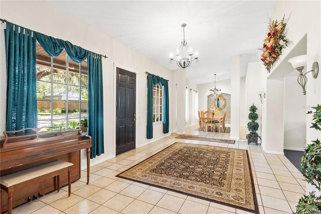 A tiled entryway features a piano, a large area rug, and a view into the dining — 81 N CAROL AVENUE, MASCOTTE, FL