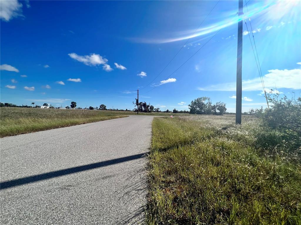 A paved road stretches through an open, grassy field under a bright blue sky — 4 WINDWARD LANE, PLACIDA, FL