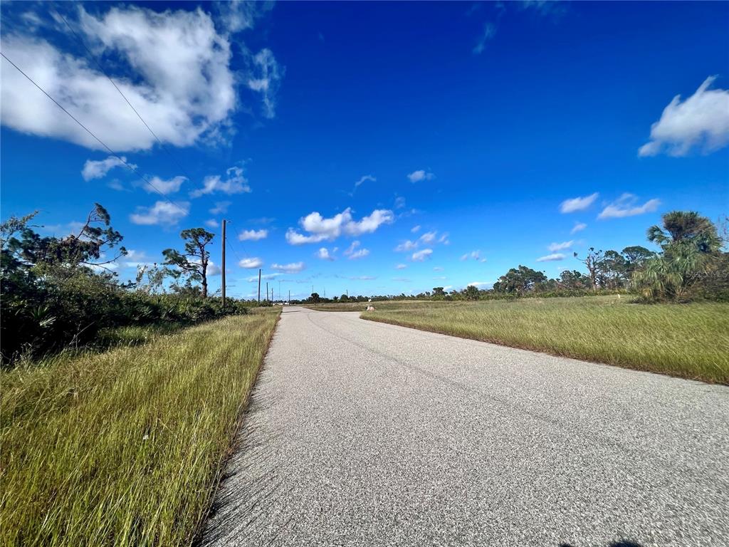 An asphalt road stretches through a grassy, undeveloped lot under a bright blue sky — 4 WINDWARD LANE, PLACIDA, FL
