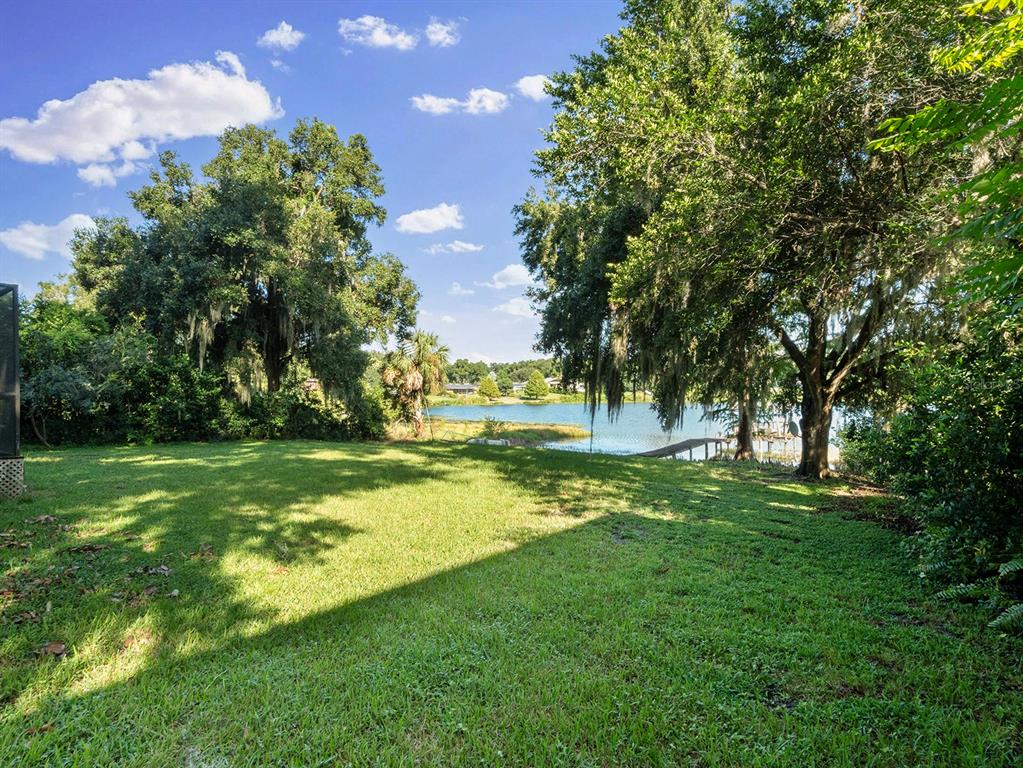 A grassy backyard leads to a lake with a wooden dock under large shade trees — 2813 TIMBERLAKE DRIVE, ORLANDO, FL