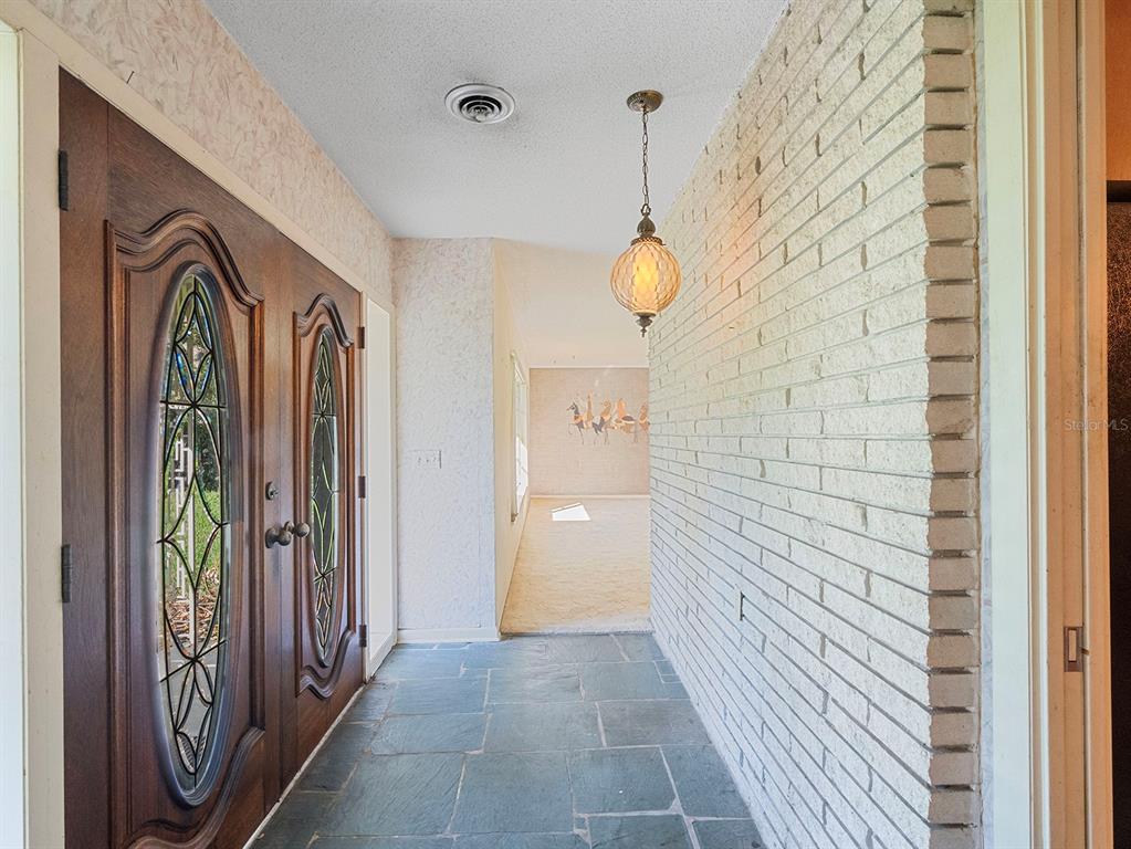 An entryway features a slate floor, a brick wall, and a double wooden front door — 2813 TIMBERLAKE DRIVE, ORLANDO, FL