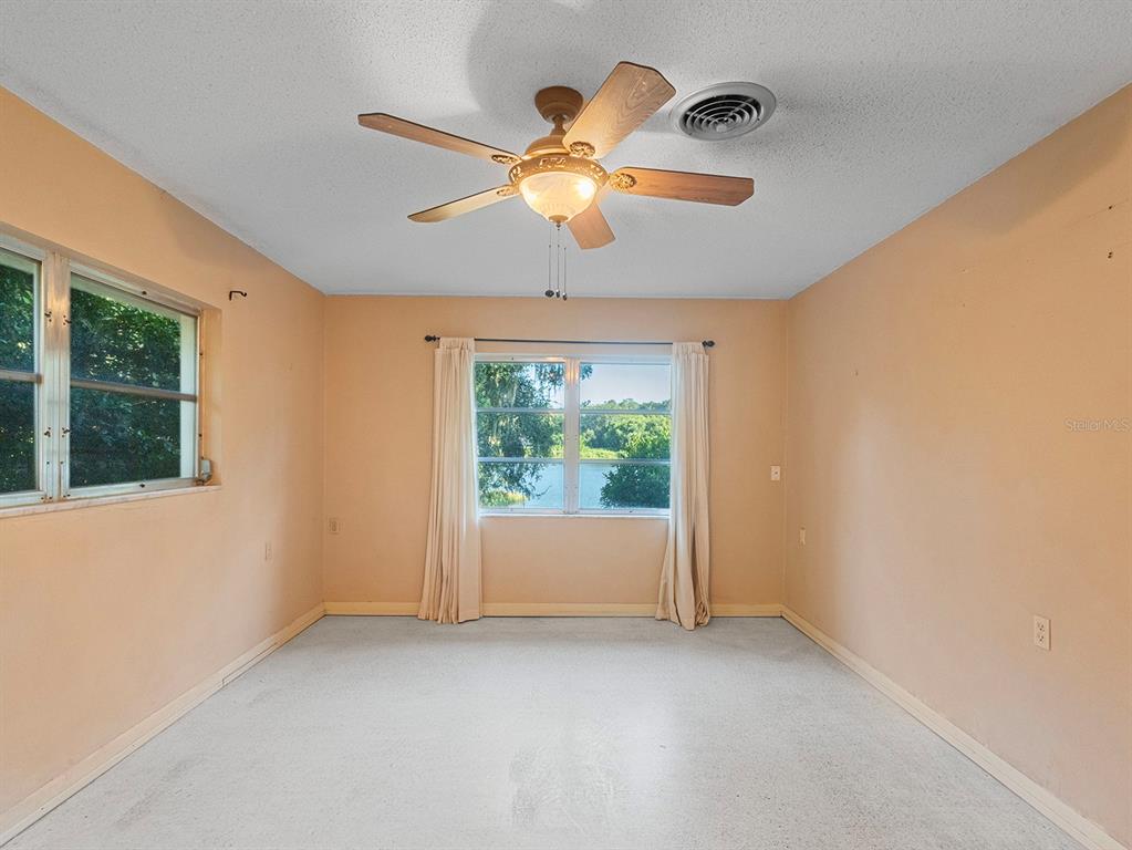 A bedroom with peach walls, a ceiling fan, white carpeting, and a view of trees — 2813 TIMBERLAKE DRIVE, ORLANDO, FL