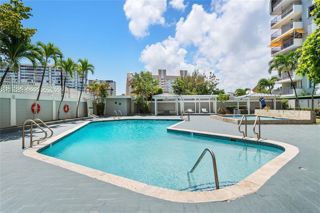 An outdoor swimming pool with a stone deck, palm trees, and a multi-story apartment building — 801 CANGREJO ARRIBA UNIT 801 A, CAROLINA, PR