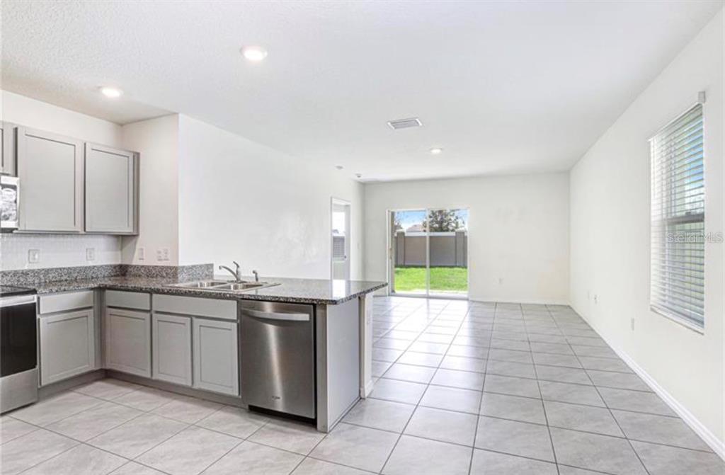 A kitchen with grey cabinets and granite countertops opens into a tiled living area — 31210 PENNY SURF LOOP, WESLEY CHAPEL, FL