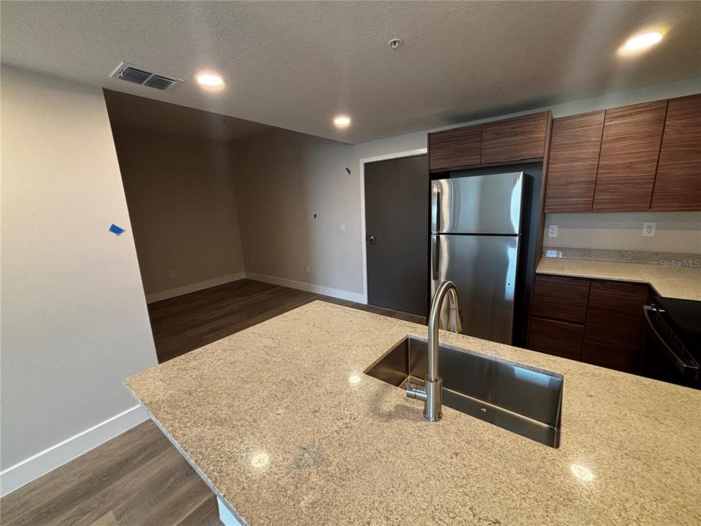 A kitchen features a granite island with a sink, stainless steel refrigerator, and wood cabinets — 4424 S TEXAS AVENUE UNIT 210, ORLANDO, FL