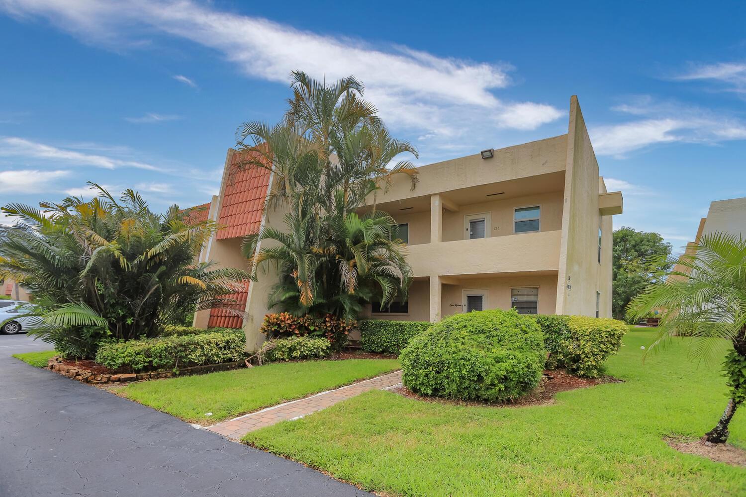 A two-story apartment building with a tan stucco exterior, palm trees, and a paved walkway — 2500 Fiore Way # a, Delray Beach FL 33445, DELRAY BEACH, FL