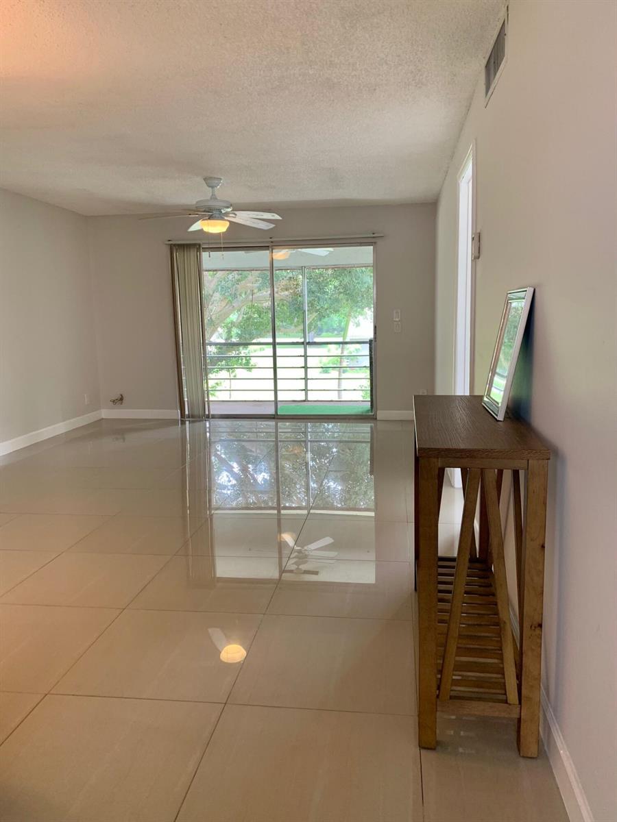 An empty living room features large light-colored floor tiles, a ceiling fan, and sliding glass doors — 2500 Fiore Way # a, Delray Beach FL 33445, DELRAY BEACH, FL