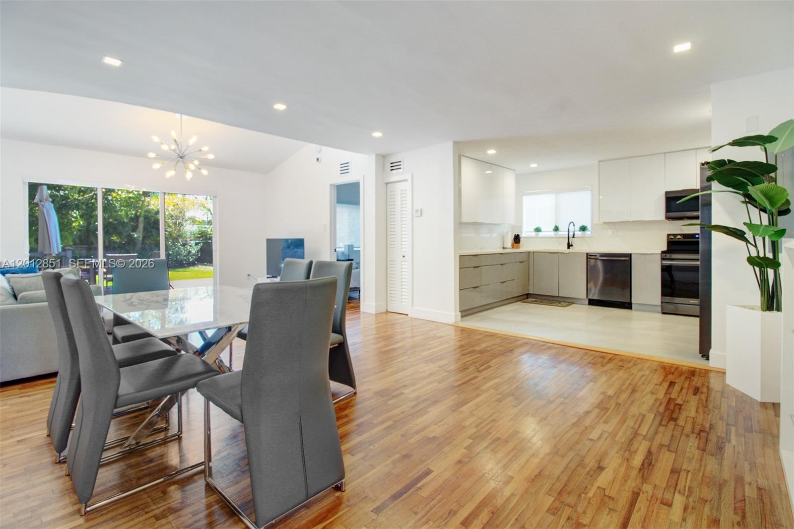 A dining area with hardwood floors transitions into a modern kitchen with white cabinetry — 360 NE 116th ST, Miami FL 33161, MIAMI, FL