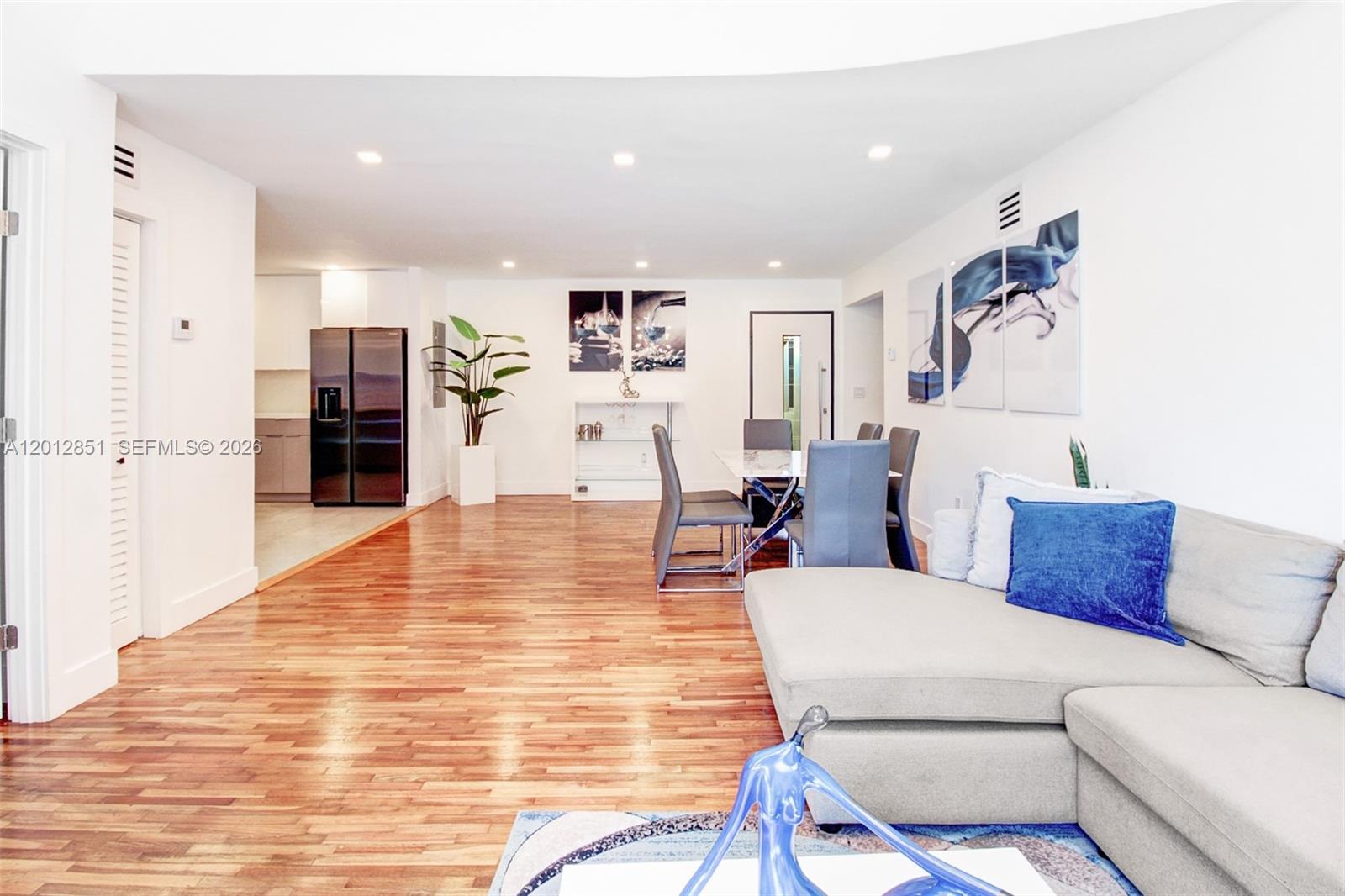 This open-concept living and dining area features hardwood floors, a sectional sofa, and modern decor — 360 NE 116th ST, Miami FL 33161, MIAMI, FL