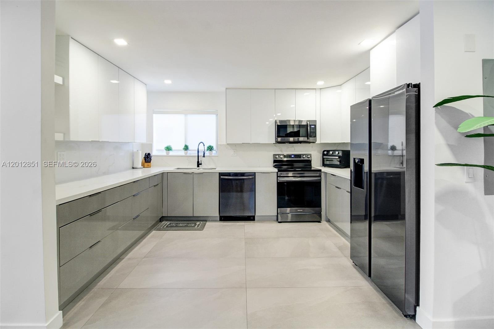 A modern kitchen features gray lower cabinets, white upper cabinets, and stainless steel appliances — 360 NE 116th ST, Miami FL 33161, MIAMI, FL
