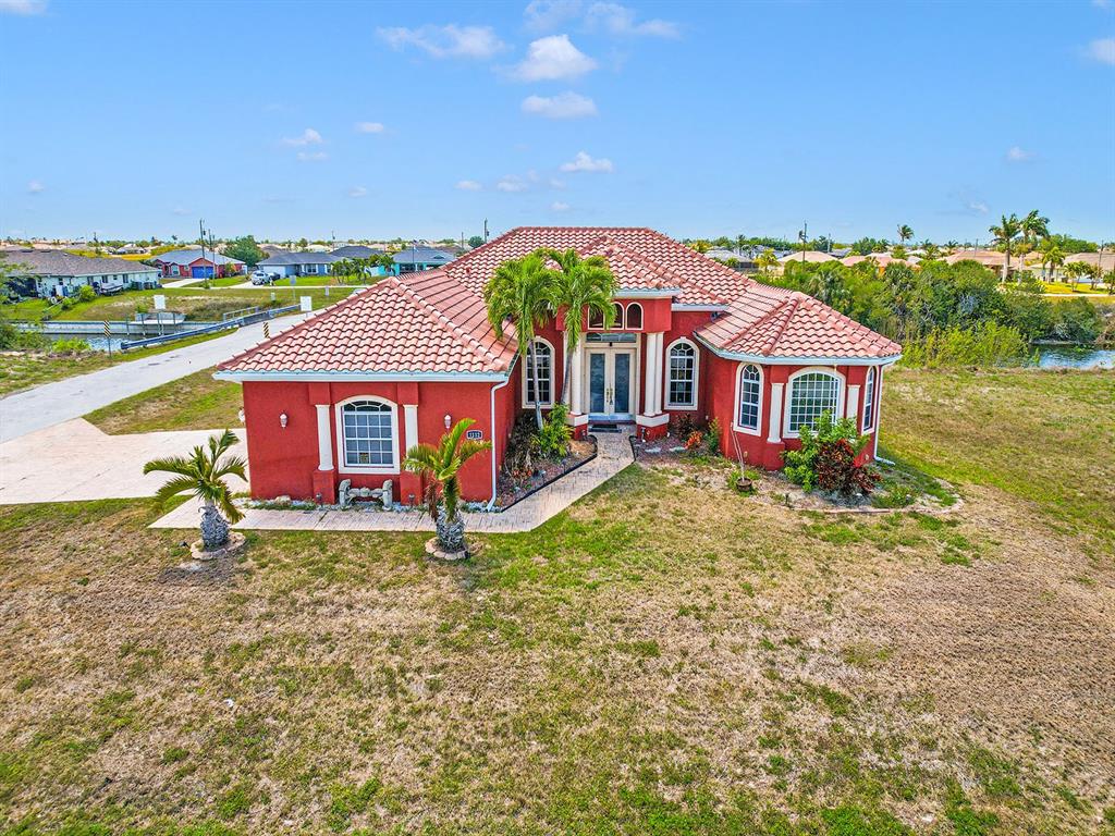 An aerial view shows a red, single-story house with a tiled roof and a paved walkway — 1112 NW 9TH AVENUE, CAPE CORAL, FL